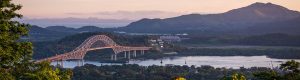Landscape photo of a bridge over a river and mountains in the distance.